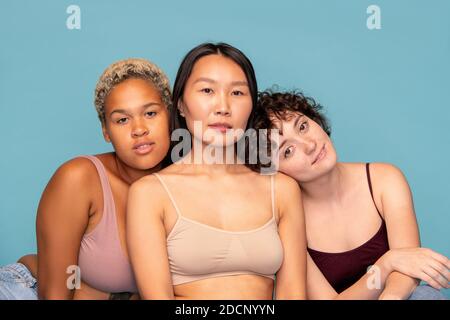 Three affectionate and friendly girls in tanktops sitting close to one another Stock Photo