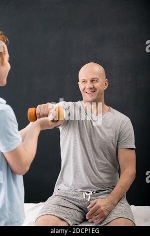 Young physiotherapist helping mature male patient with exercising in clinics Stock Photo