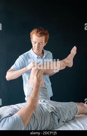Contemporary clinician holding leg bent in knee of his patient lying on couch Stock Photo