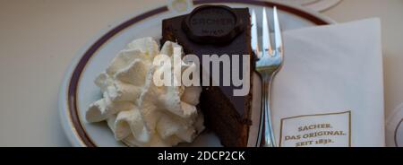 VIENNA, AUSTRIA - JULY 14, 2019:  Panorama view of slice of Sacher-Torte cake on plate at the Cafe Sacher with branded napkin Stock Photo
