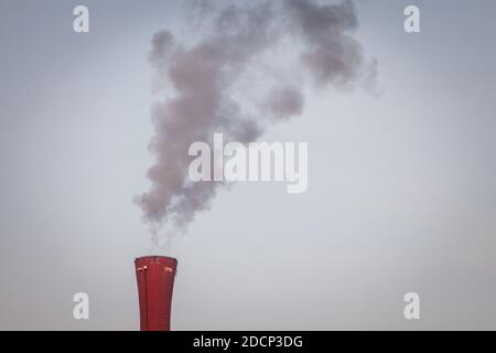 Industrial red chimney of a factory working and releasing toxic fume and smokes in the atmosphere.   Picture of the chimney of a factory releasing fum Stock Photo