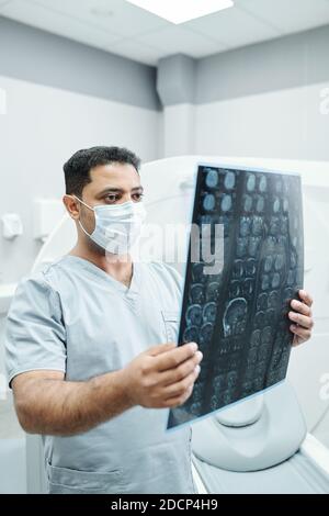 Serious mature mixed-race radiologist in mask and uniform analyzing x-ray image Stock Photo