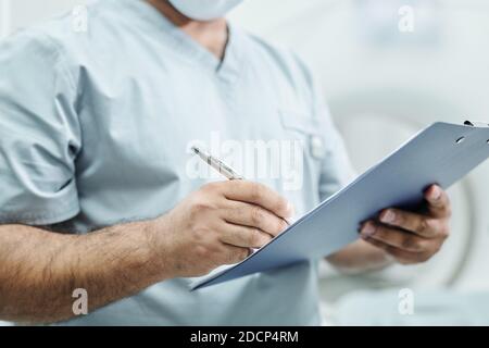 Hands of mature mixed-race male doctor in uniform making notes in document Stock Photo