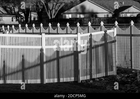 Black & white view of white vinyl picket style fence and shadows; Salida; Colorado; USA Stock Photo