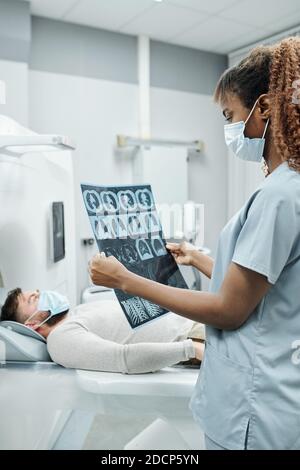 Young African female radiologist in uniform and mask analyzing x-ray image Stock Photo