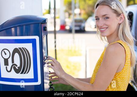 happy female driver checking air pressure of car tire outdoors Stock Photo