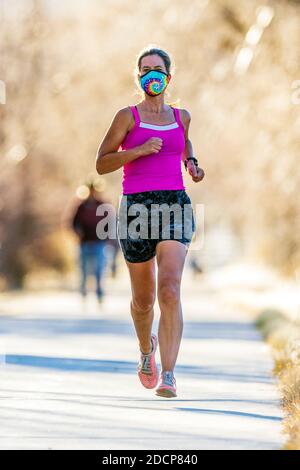 Attractive; fit; middle-aged woman wearing protective face mask; running on paved trail; Salida; Colorado; USA Stock Photo