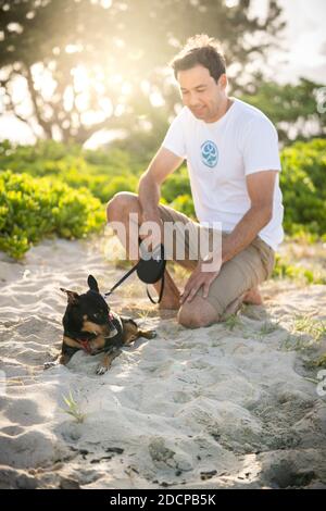 Young fit male squats on the beach with his small black dog in Hawaii Stock Photo