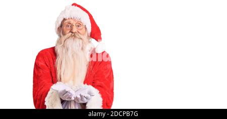 Old senior man with grey hair and long beard wearing traditional santa claus costume smiling with hands palms together receiving or giving gesture. ho Stock Photo