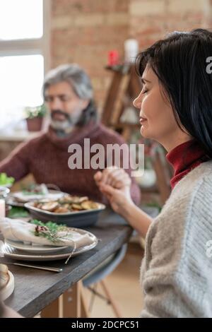 Hands of mature woman and bearded man with closed eyes praying before dinner Stock Photo