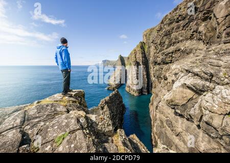 Side view of unrecognizable male explorer standing on rocky cliff and admiring sea Stock Photo
