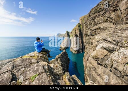 Side view of anonymous male traveler taking photo of cliff near sea during vacation Stock Photo