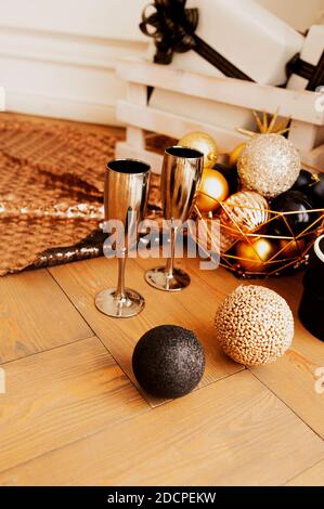 two metal gold drinking glasses on wooden floor with decorations for Christmas in gold and black tones: round shiny balls, gift boxes, garlands and sh Stock Photo
