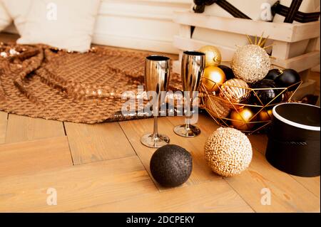 two metal gold drinking glasses on wooden floor with decorations for Christmas in gold and black tones: round shiny balls, gift boxes, garlands and sh Stock Photo