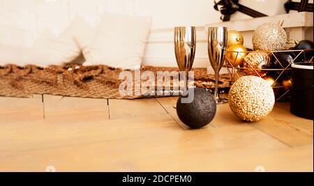 Christmas banner, two metal gold drinking glasses on wooden floor with decorations in gold and black tones: round shiny balls, gift boxes, shining bro Stock Photo