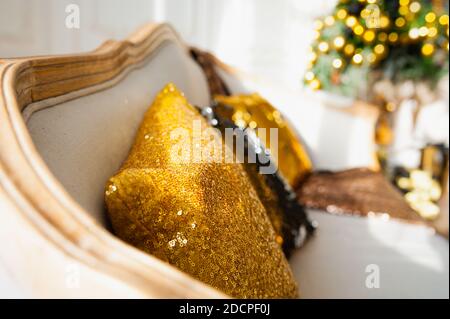 Gold shining decorative pillow with sequins on a beige sofa, garland and bokeh on Christmas interior on background, . Christmas decor for the home. Stock Photo