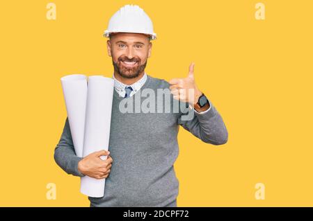 Handsome middle age man holding paper blueprints smiling happy and positive, thumb up doing excellent and approval sign Stock Photo