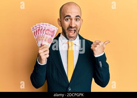 Hispanic bald business man holding 100 yuan chinese banknotes screaming proud, celebrating victory and success very excited with raised arm Stock Photo