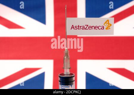 Stafford / United Kingdom - November 22 2020: AstraZeneca Oxford vaccine Covid-19 concept. Syringe needle and sticker on it, blurred UK flag on the ba