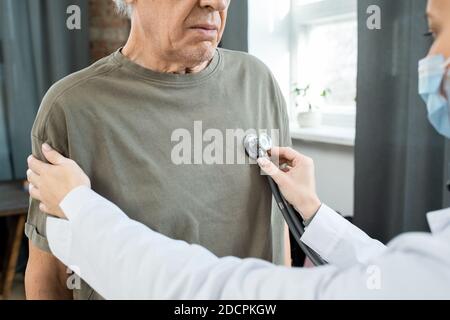 Hands of young female doctor in whitecoat examining breath of sick senior man Stock Photo
