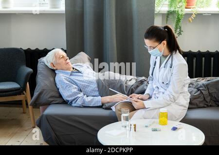 Young doctor using tablet to fill in electronic sick leave of senior man Stock Photo