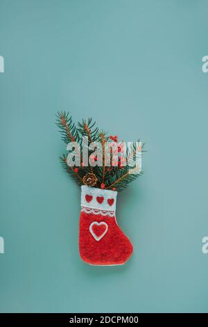 Greeting card mockup with Christmas decorative handmade felt sock with spruce branches and dry berries and cone on trendy muted green background Stock Photo