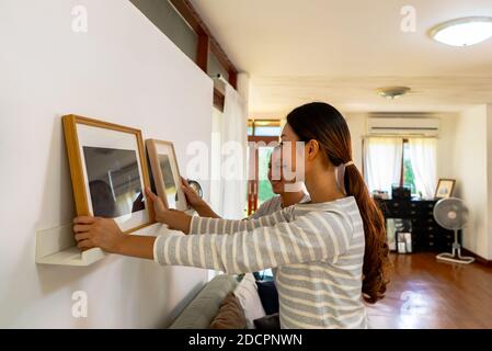 Young couple hanging picture frame on wall in their new house. Smiling husband and wife happy settling together in newly owned home Stock Photo