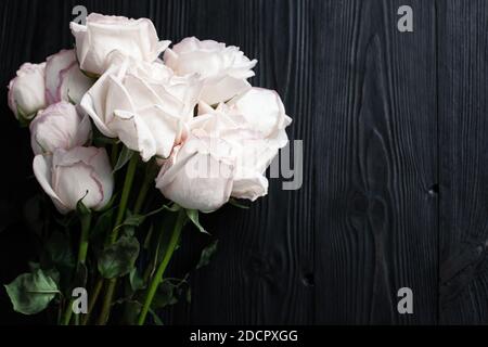 Delicate white roses on black wooden background close up, beautiful light pink flowers bouquet on dark gray wood, birthday greeting card, wedding Stock Photo