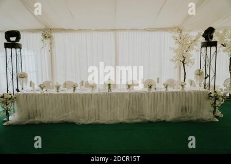A modern table set-up with white skirting cloth and flowers in a wedding reception Stock Photo