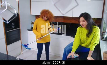 Two young women having fun while doing house cleaning. Multiracial friendship or relationship. High quality photo Stock Photo