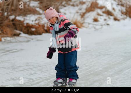 Little school girl skating on the frozen lake on a cloudy winter day Stock Photo
