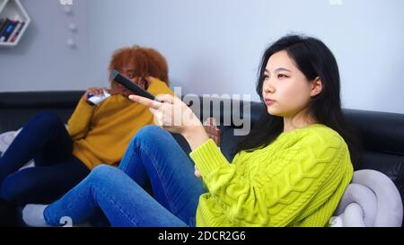 Bored rommates, students sitting on the couch watching television gossiping and eating chocolates. High quality photo Stock Photo