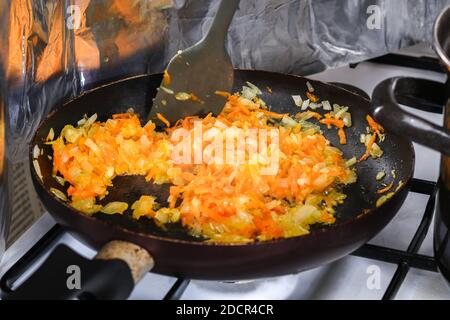 Frying carrots and onions for soup in a pan. The man is stirring the frying with a silicone spatula.
