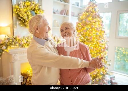 Senior couple dancing near new year tree and looking in love Stock Photo