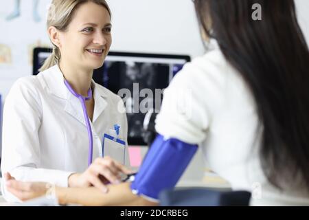 Smiling doctor measuring blood pressure to woman patient in clinic Stock Photo
