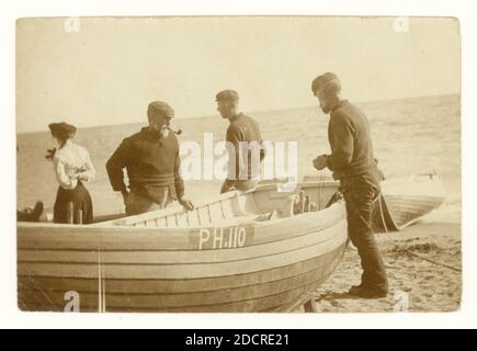 Original early 1900's sepia toned photograph group of fishermen beside their boats which are pulled up on the shore, preparing to go to sea, possibly line fishing, registered in Plymouth as PH 110,  Devon, U.K. circa 1910 Stock Photo