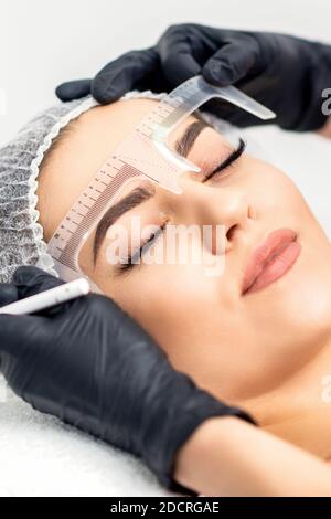 Beautician is measuring the brows with ruler before tattooing eyebrows Stock Photo