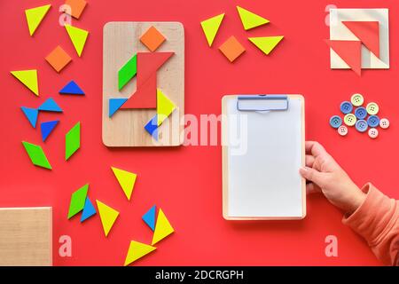 Creative design, Autism World Day, writing pad in hand. Tangram puzzle, flat lay on red, pictogram Stock Photo