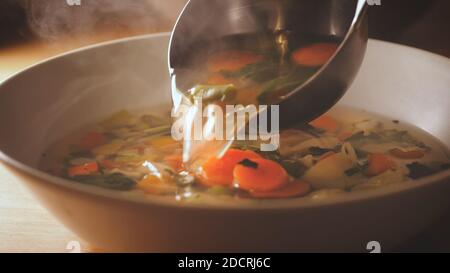 Pour a ladle of minestrone soup. Vegetarian soup dish is on table. Vegetarian healthy meal for dinner. Ready vegetable meal for lunch, hot and cozy so Stock Photo