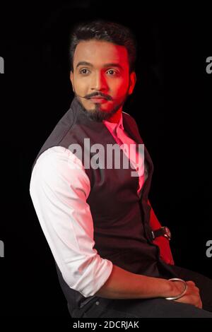 Young bearded man in formal waistcoat looking sideway. Black background. Red lighting on face Stock Photo