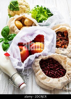 Fresh fruits and vegetables in eco cotton bags on table in the kitchen. Milk,  potatoes, apricots, rucola, beans from market. zero waste shopping conc Stock Photo