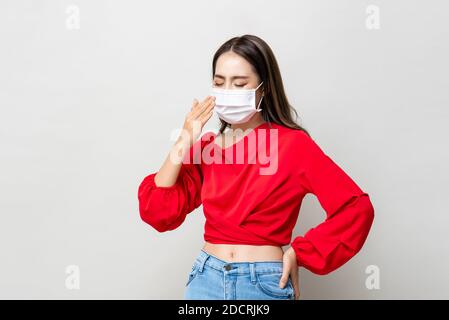 Asian woman wearing medical face mask coughing on light gray isolated background