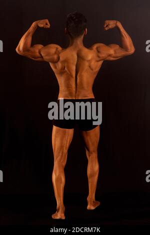 Muscular bodybuilder male in gym. Black background. Back profile. Full length shot Stock Photo