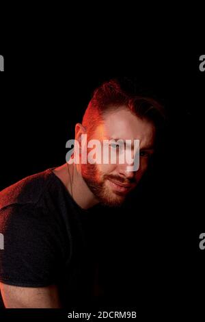 A brutal man on a dark background in the light of a red lamp Stock Photo