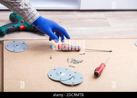 Male hands in gloves, master collects table furniture using screwdriver tools, instrument at home. Furniture assembly using screwdriver. Moving, home Stock Photo