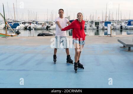 Young happy couple roller skating in skate park next to the beautiful port in summer.Friendship sport and fitness lifestyle concept.