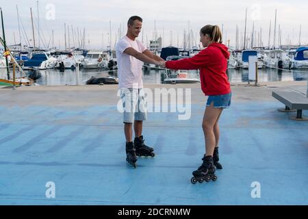 Young beautiful couple roller skating in skate park next to the amazing port in summer.Friendship sport and healthy lifestyle concept. Stock Photo