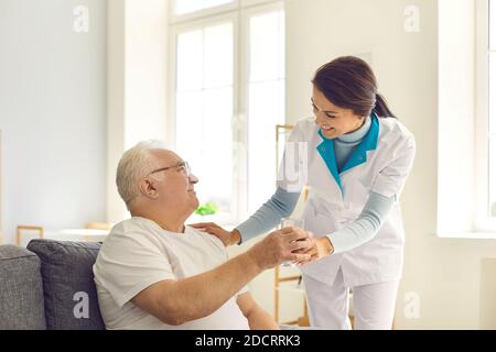 Smiling nurse giving glass of water to senior man in nursing home or assisted living facility Stock Photo