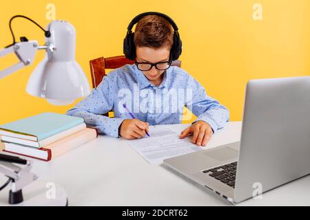 schoolboy in headphones, doing homework using a laptop computer, learning through an online e-learning system. coronavirus, online school Stock Photo
