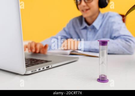 schoolboy sits at a Desk and uses a laptop, on a yellow background. Distance learning, quarantine, coronavirus Stock Photo